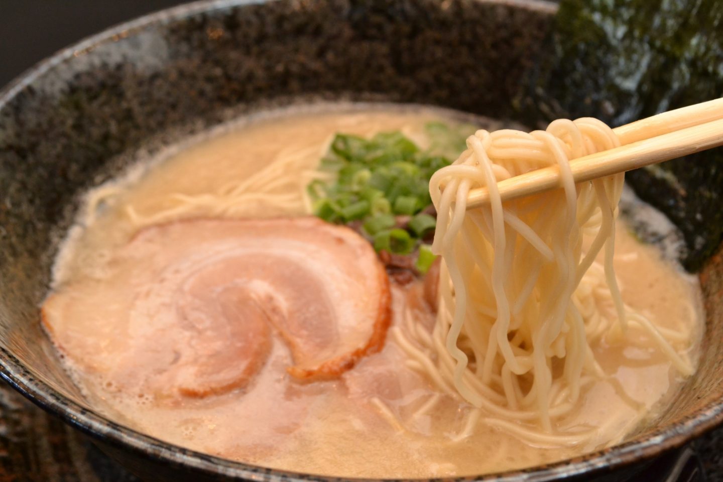 Essstäbchen greifen eine Portion Nudeln aus einer Schüssel Ramen