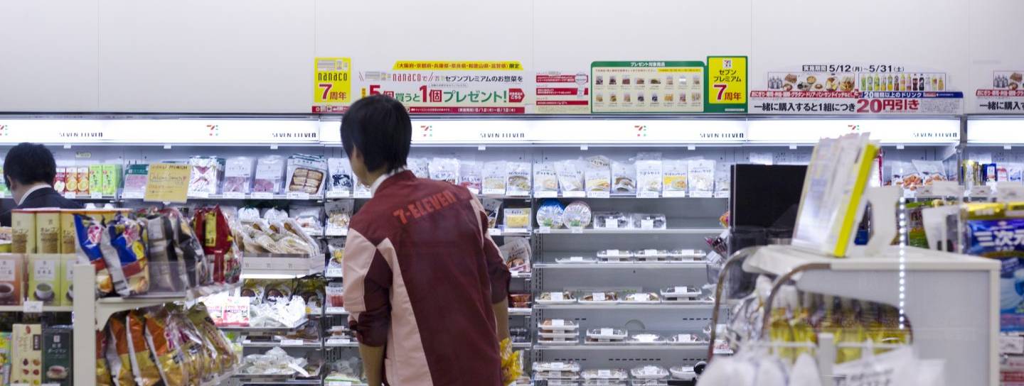 Ein Mitarbeiter in einem Seven Eleven in Japan von hinten vor den Regalen
