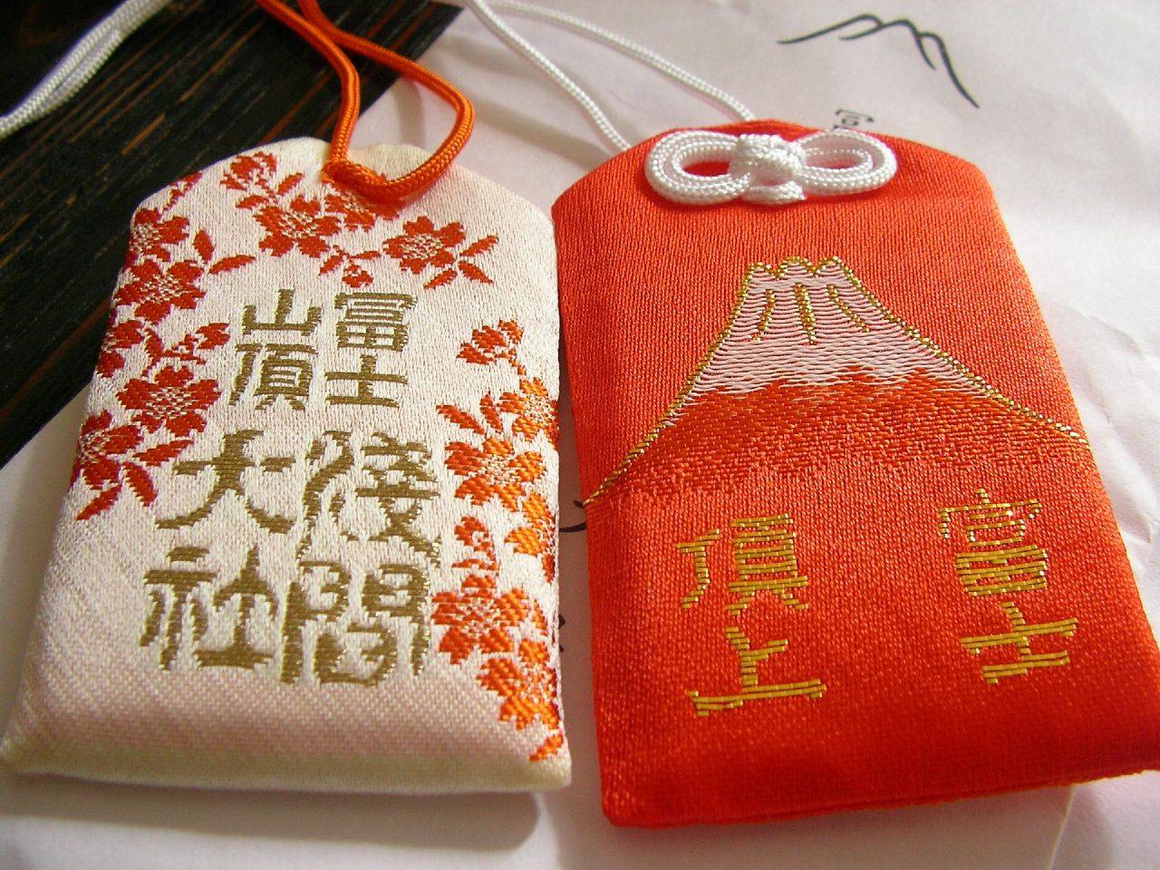 Zwei O-Mamori (Glücksbringer) mit Blüten- und Fuji-Motiv