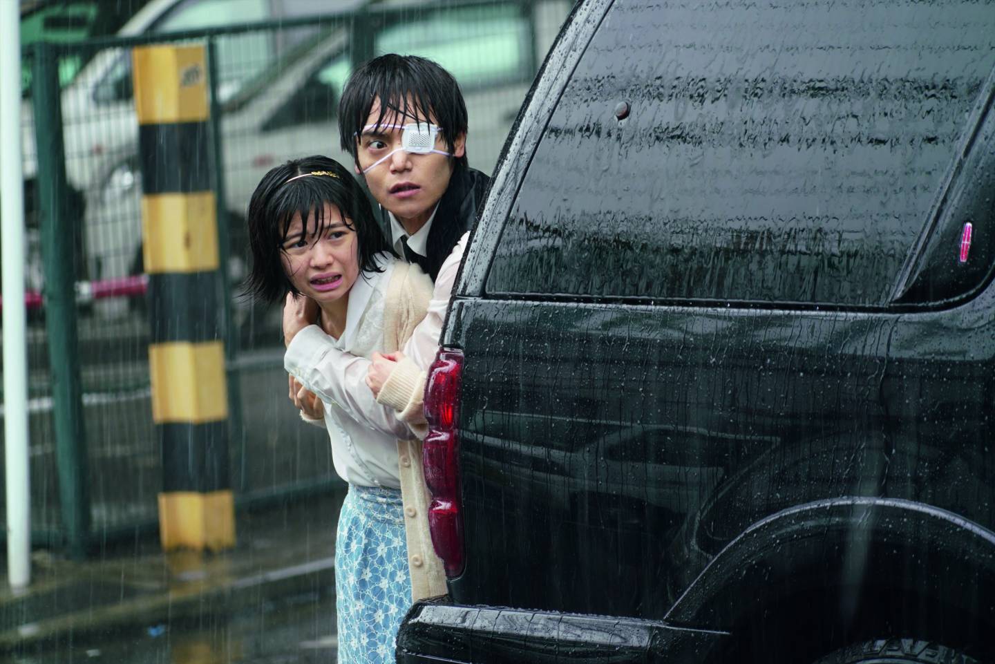 Filmausschnitt Tokyo Ghoul: Mann und Mädchen kauern hinter Auto im Regen