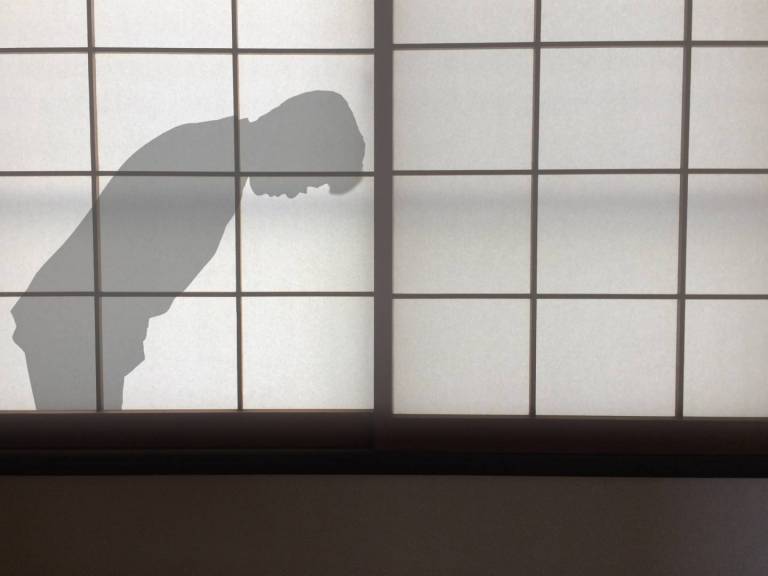Shilouette eines sich verbeugenden Manns hinter einem Papierfenster