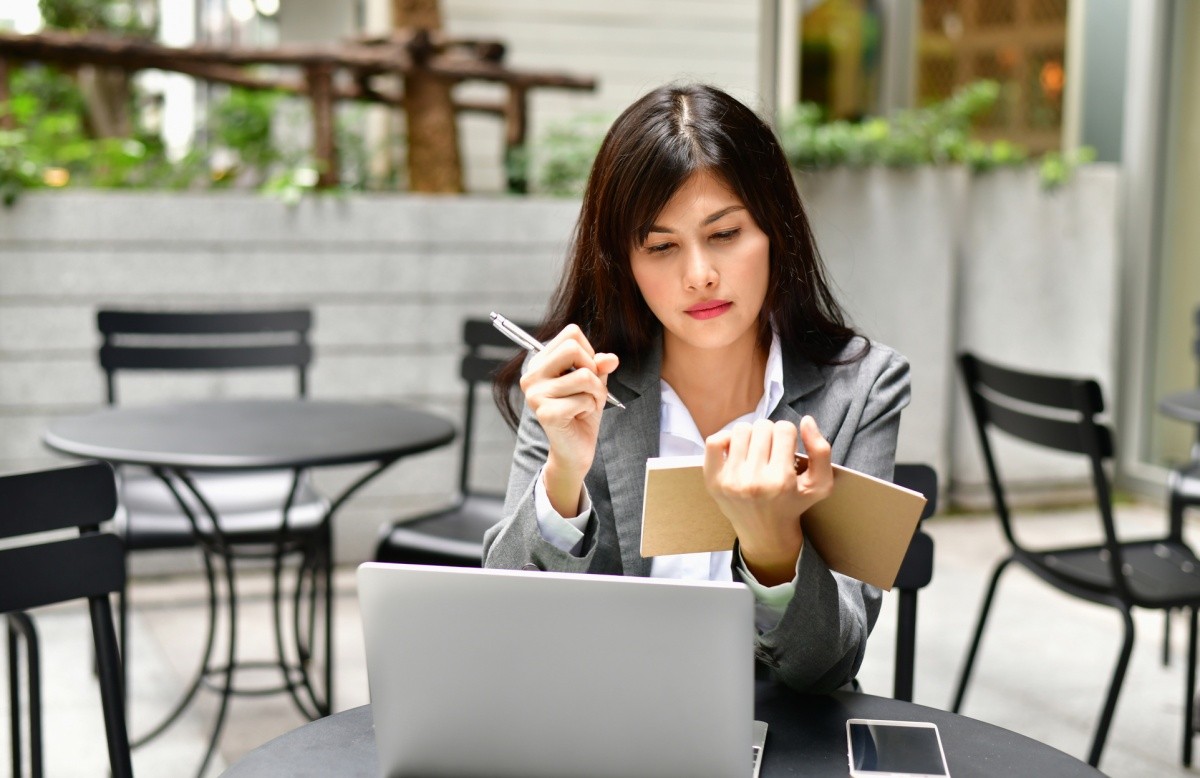 Frau mit Notizbuch, vor ihr ein Laptop auf einem Tisch