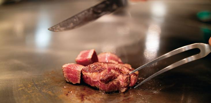 Nahhaufnahme von Fleisch auf einer heißen Grillplatte mit Messer