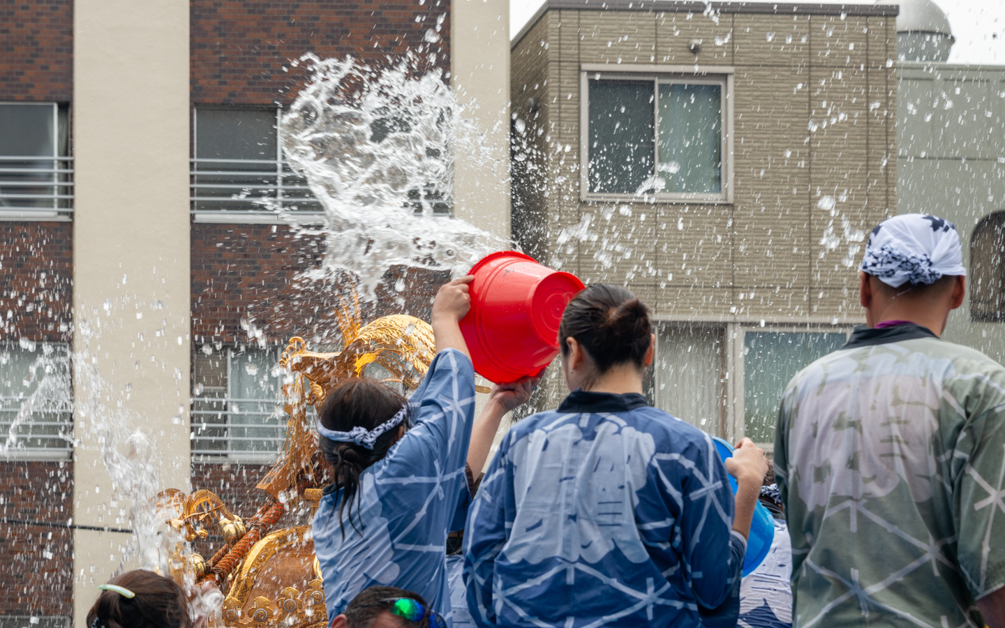 Menschen schütten Wasser auf eine Schreinparade bei einem Fest