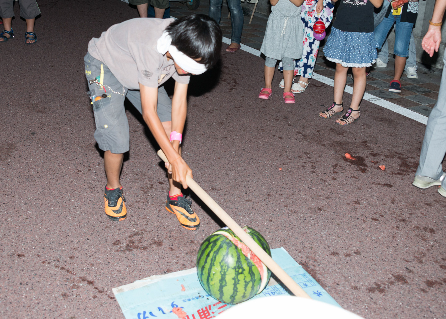 japanischer Junge mit verbundenen Augen zerschlägt Wassermelone bei einem Fest