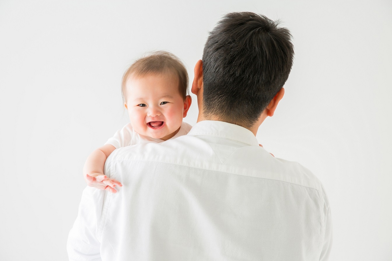 Mann von hinten mit einem Baby auf dem Arm, das in die Kamera lacht