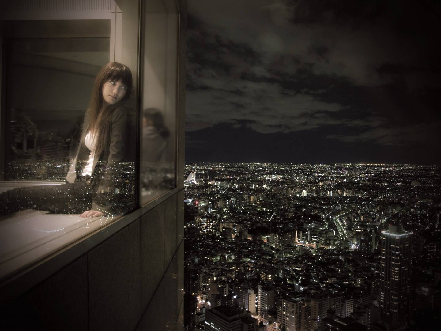 Japanische Frau, die bei Nacht aus einem Hotelfenster auf das Stadtpanorama schaut