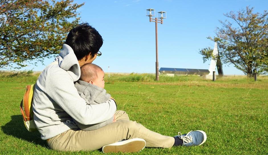 Vater auf einer Wiese mit Baby im Arm