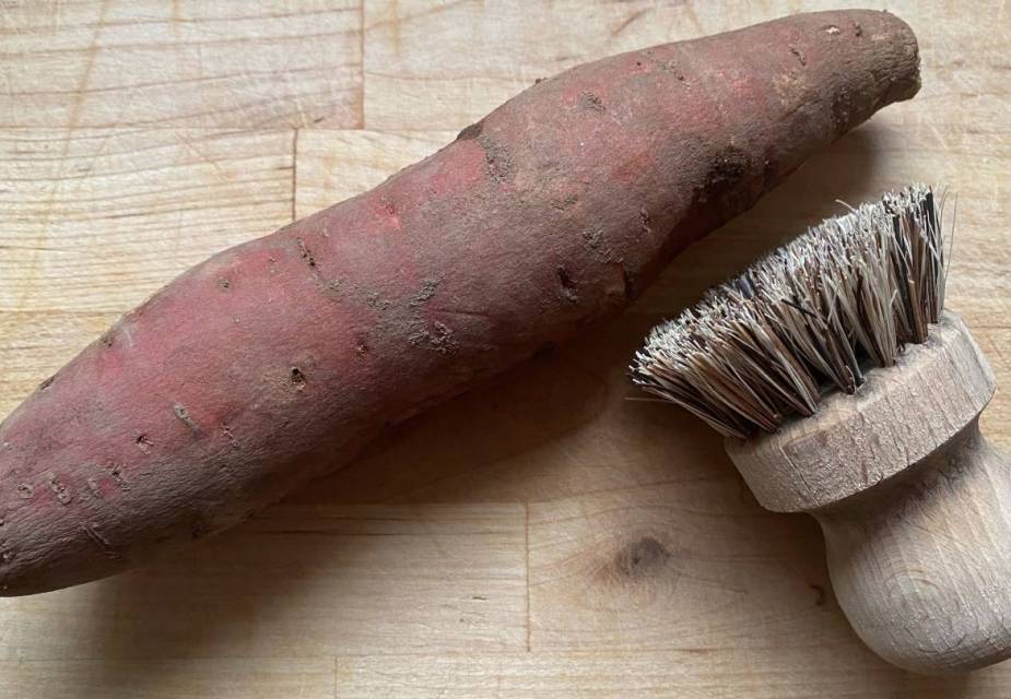 Ungeschälte Süßkartoffeln auf Holztisch, Bürste mit Holzgriff