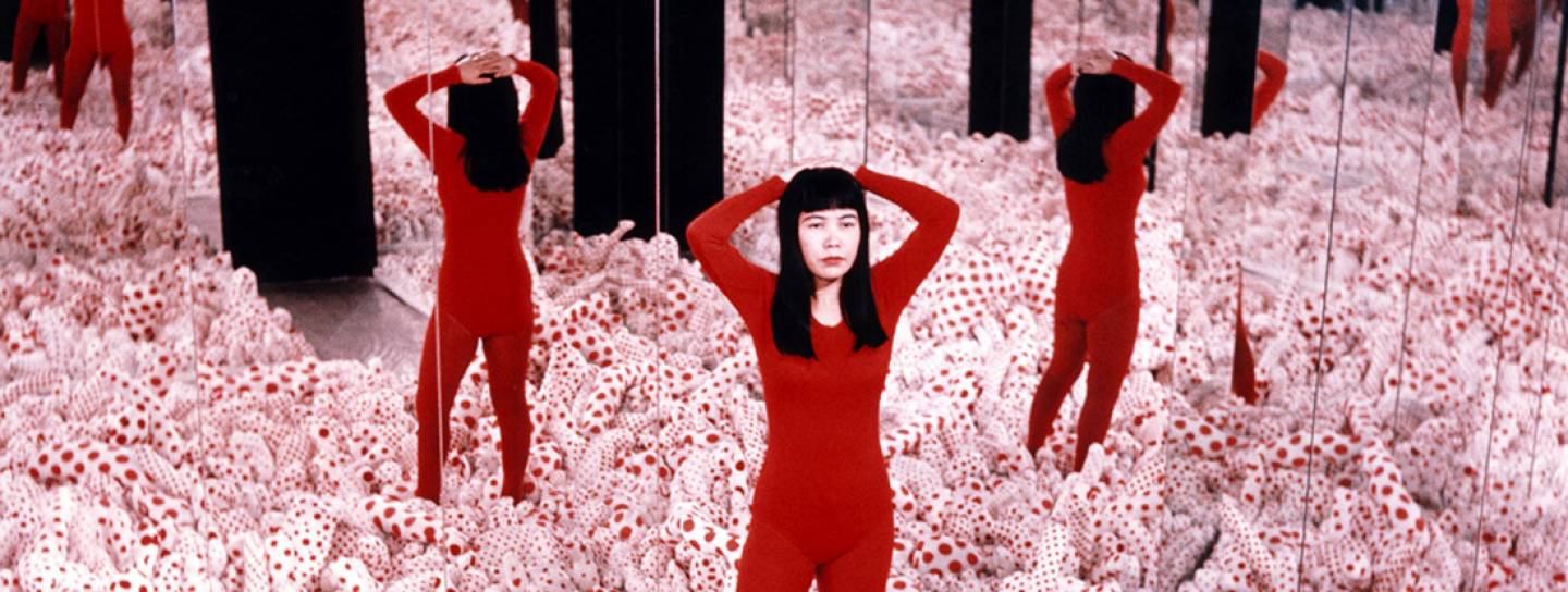 Künstlerische Installation von Kusama Yayoi in einem Spiegelraum mit rotem Kostüm und Polka Dots