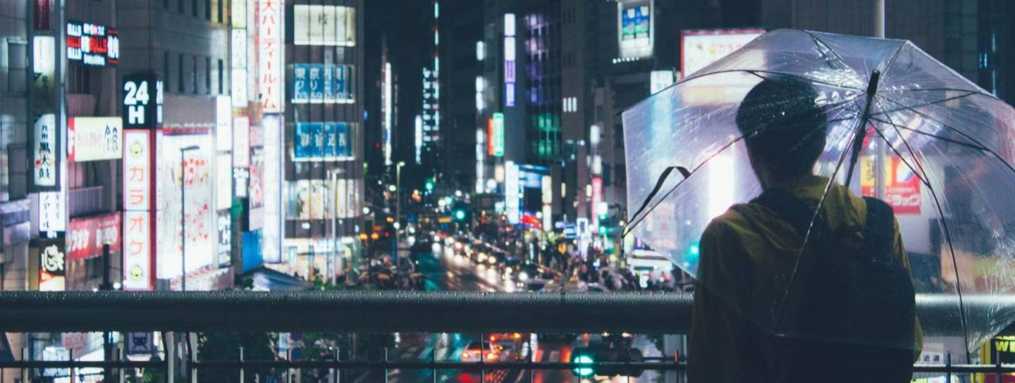 Mann mit Regenschirm blickt auf die Lichter von Shinjuku