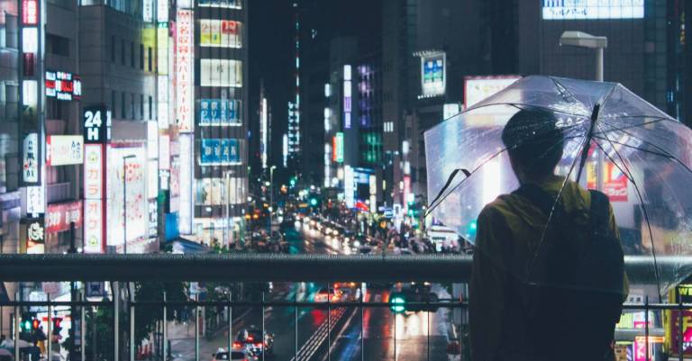 Mann mit Regenschirm blickt auf die Lichter von Shinjuku