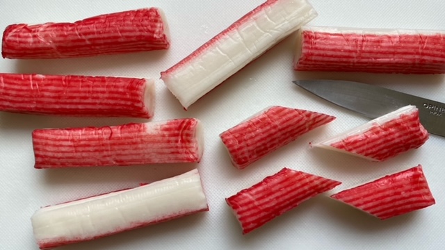 Surimi (Krabbenfleischimitat) wird auf einem Schneidebrett schräg halbiert