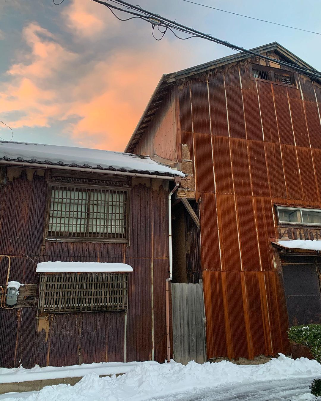 Alte Häuser in typischer, rostbrauner Farbe vor rötlichem Himmel in Aoya