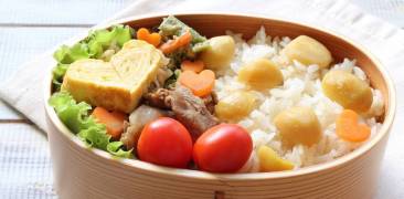 Bento-Box mit Rührei in Herzform, Salat, Tomaten und Reis mit Kastanien
