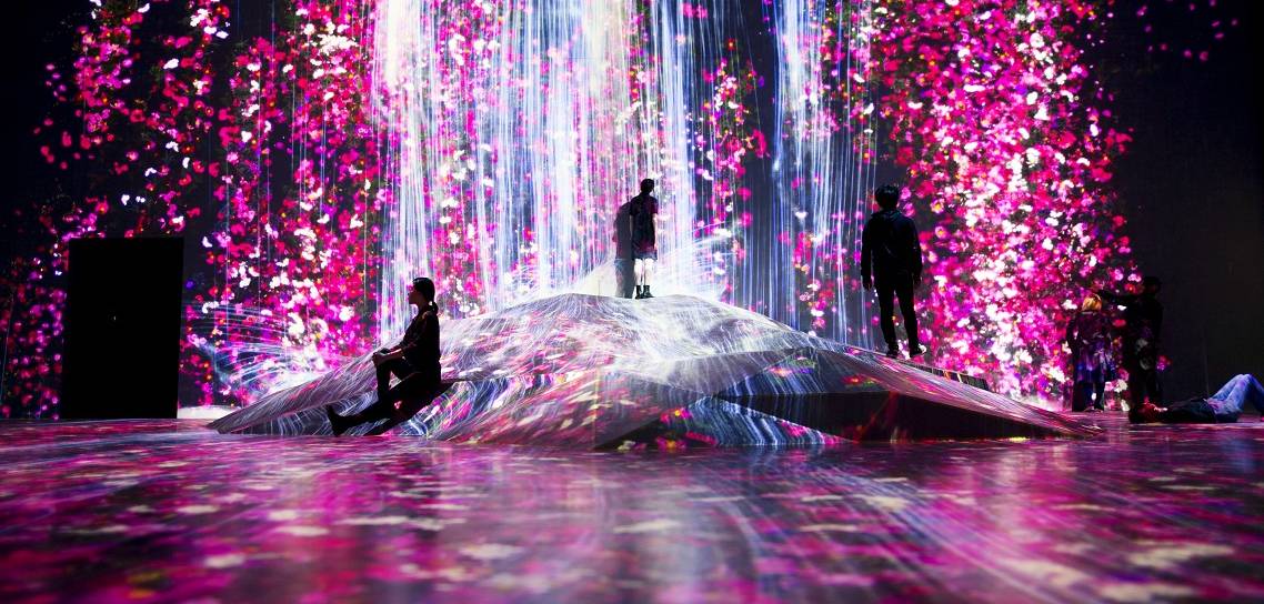 Ausstellung teamLab Borderless, pink-blaue Lichtinstallation mit staunenden Besuchern