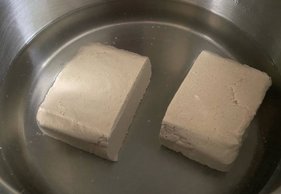 Zwei Hälften Tofu werden in heißem Wasser gekocht