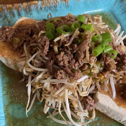 Mungbohnen auf Tofu angerichtet mit Hackfleisch und Frühlingszwiebeln auf türkisem, eckigem Teller