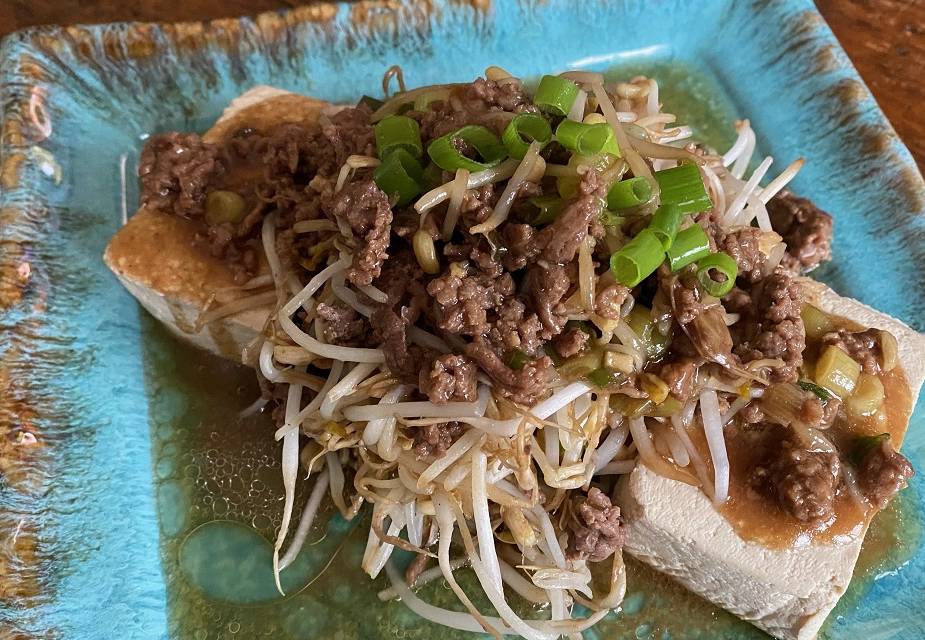 Mungbohnen auf Tofu angerichtet mit Hackfleisch und Frühlingszwiebeln auf türkisem, eckigem Teller