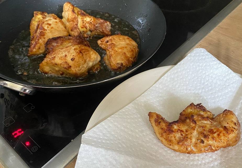 Hähnchenbruststücke werden mit Stäbchen aus der Pfanne genommen und auf Küchenpapier gelegt