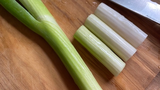 Dicke Frühlingszwiebeln auf Schneidebrett, teils geschnitten