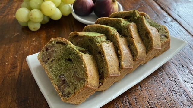 Matcha-Kuchen auf Teller angerichtet mit Weintrauben und Feigen im Hintergrund