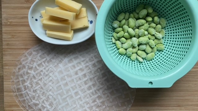 Edamame in türkisblauem Sieb und Bergkäse auf kleinem blaugepunktetem Teller