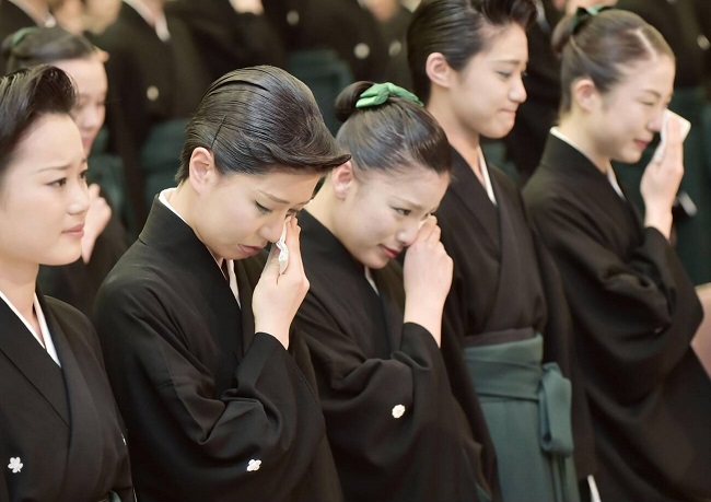 Absolventinnen der Takarazuka Music School schluchzend in schwarzen Roben bei der Abschlusszeremonie