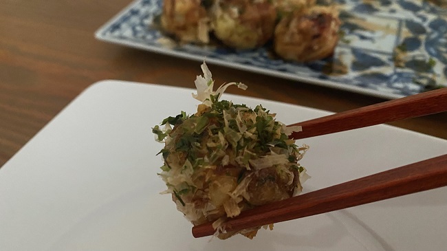 Fertiges Takoyaki-Bällchen wird mit Esstäbchen gehalten