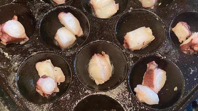 Oktopusstücke werden gleichmäßig in die Mulden der Takoyaki-Pfanne gegeben