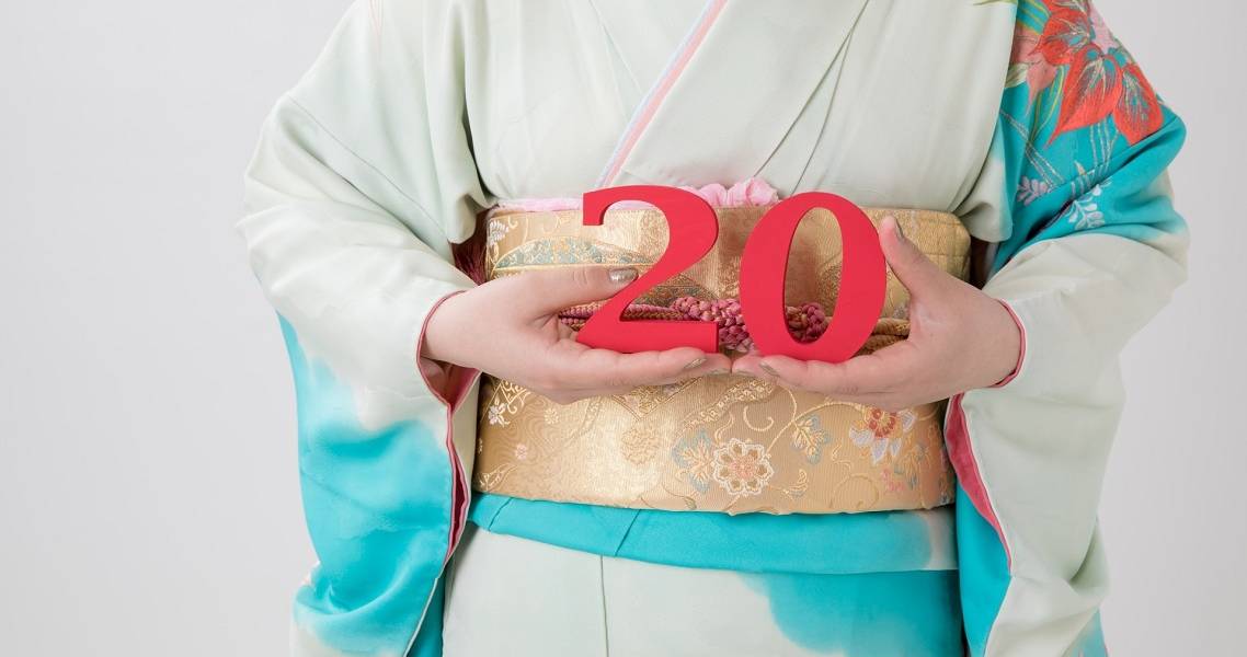 Japanerin im Kimono hält eine rote "20" hoch