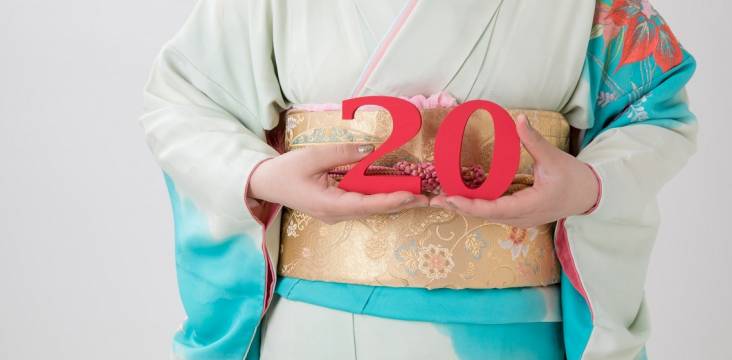 Japanerin im Kimono hält eine rote "20" hoch