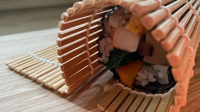 Sushi wird mithilfe der Bambusmatte aufgerollt