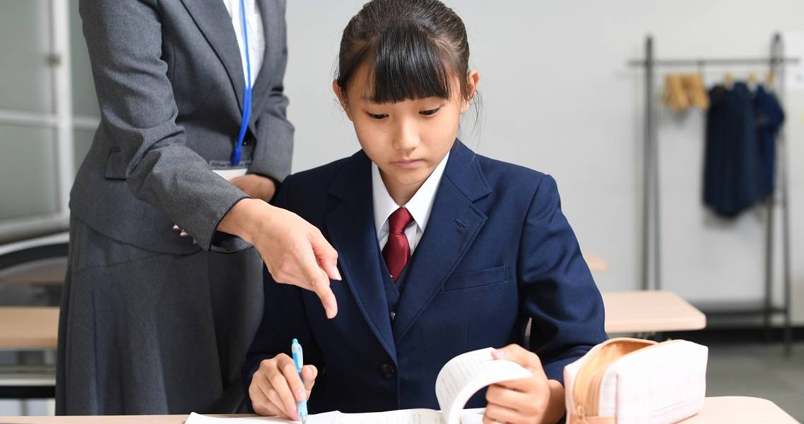 Japanische Schülerin wird von einer Lehrerin beim Lernen angeleitet