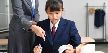 Japanische Schülerin wird von einer Lehrerin beim Lernen angeleitet