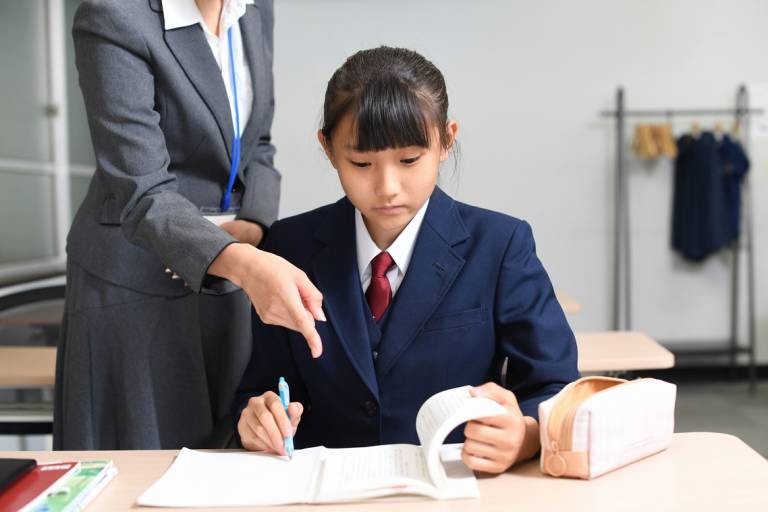 Japanische Schülerin wird von einer Lehrerin beim Lernen angeleitet