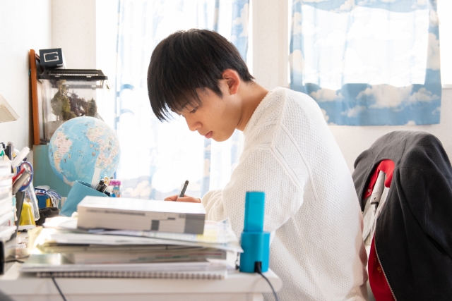 Japanischer Oberschüler am Schreibtisch zwischen Büchern beim Lernen