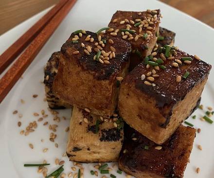 Gebratener Tofu mit Teriyaki-Sauce serviert auf weißem Teller mit Esstäbchen