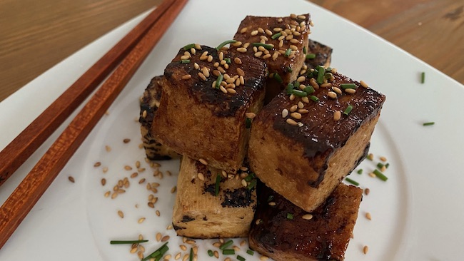 Gebratener Tofu mit Teriyaki-Sauce serviert auf weißem Teller mit Esstäbchen