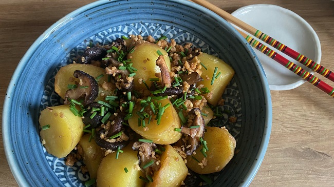 Kartoffeln mit Shiitake und Soja-Flakes serviert auf blauem Teller mit Schnittlauch garniert, daneben kleiner weißer Teller mit Stäbchen