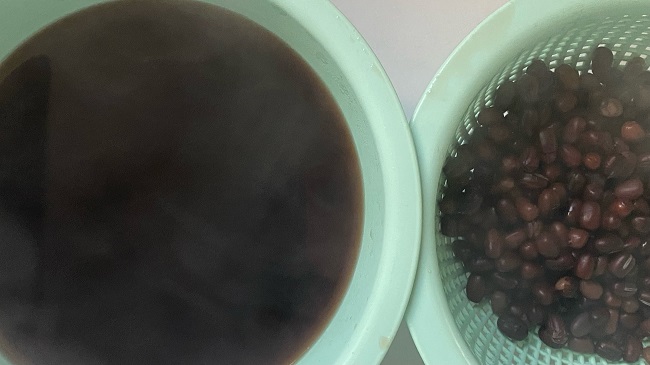 Rotverfärbtes Azuk-Bohnen-Kochwasser neben herausgenommenen Azuki-Bohnen im Sieb