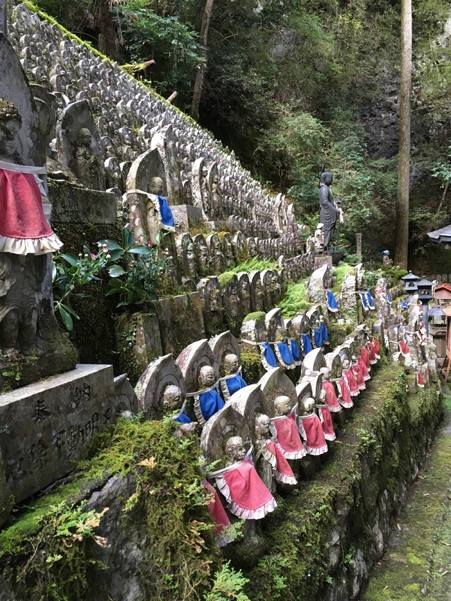 Eine große Ansammlung kleiner Jizo-Statuen mit blauen und roten Gewändern auf Steintreppen auf dem heiligen Berg Kōya-san.