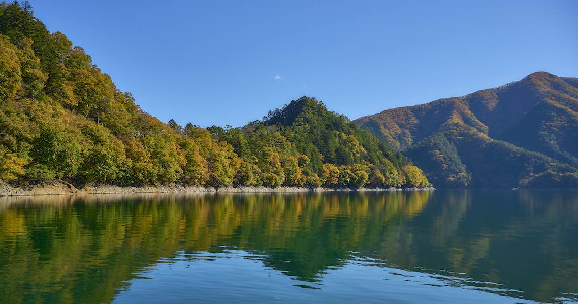 Strahlend blauer Okutama-See von Bergen umgeben