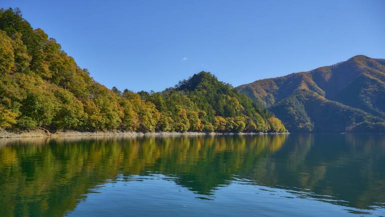 Strahlend blauer Okutama-See von Bergen umgeben