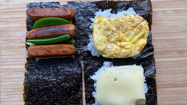 Reis, Omelett. Würstchen und Erbsenschoten auf Nori-Blatt platziert