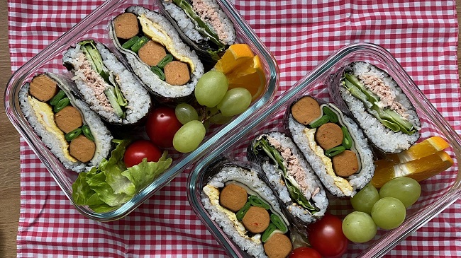 Onigirazu mit Beilagen in der Lunchbox drapiert