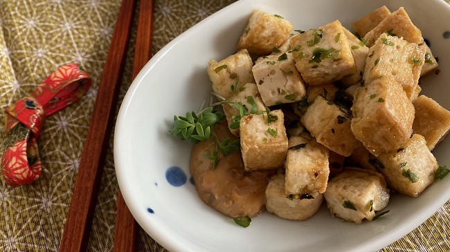 Tofuwürfel in Misonnaise auf weißem Teller serviert mit Stäbchen und japanisch gemusterter Tischdecke