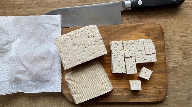 Tofu wird auf Holzbrett in Würfel geschnitten