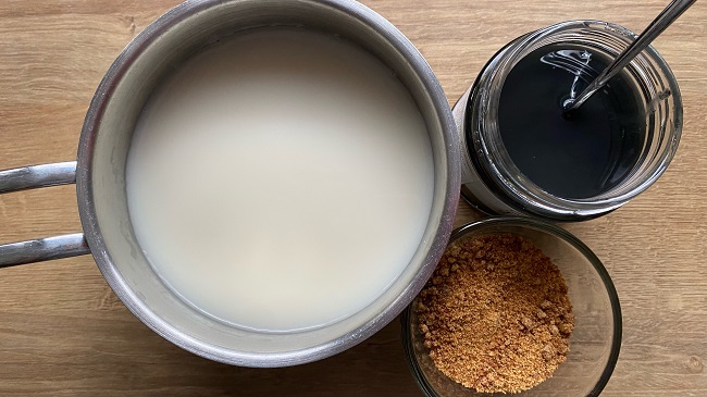Zutaten für Schwarzen Sesam-Pudding: Hafermild in einem Töpfchen, Schwarze Sesampaste im Glas und brauner Zucker im Glas