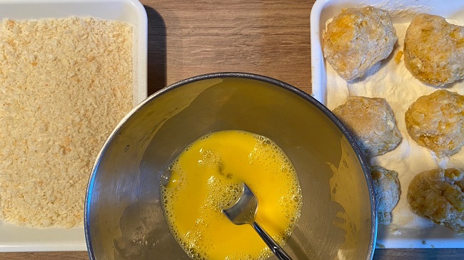 Schale mit Panko, in der Mitte eine Schüssel mit Ei-Wasser-Mischung, rechts Bällchen in einer Schale